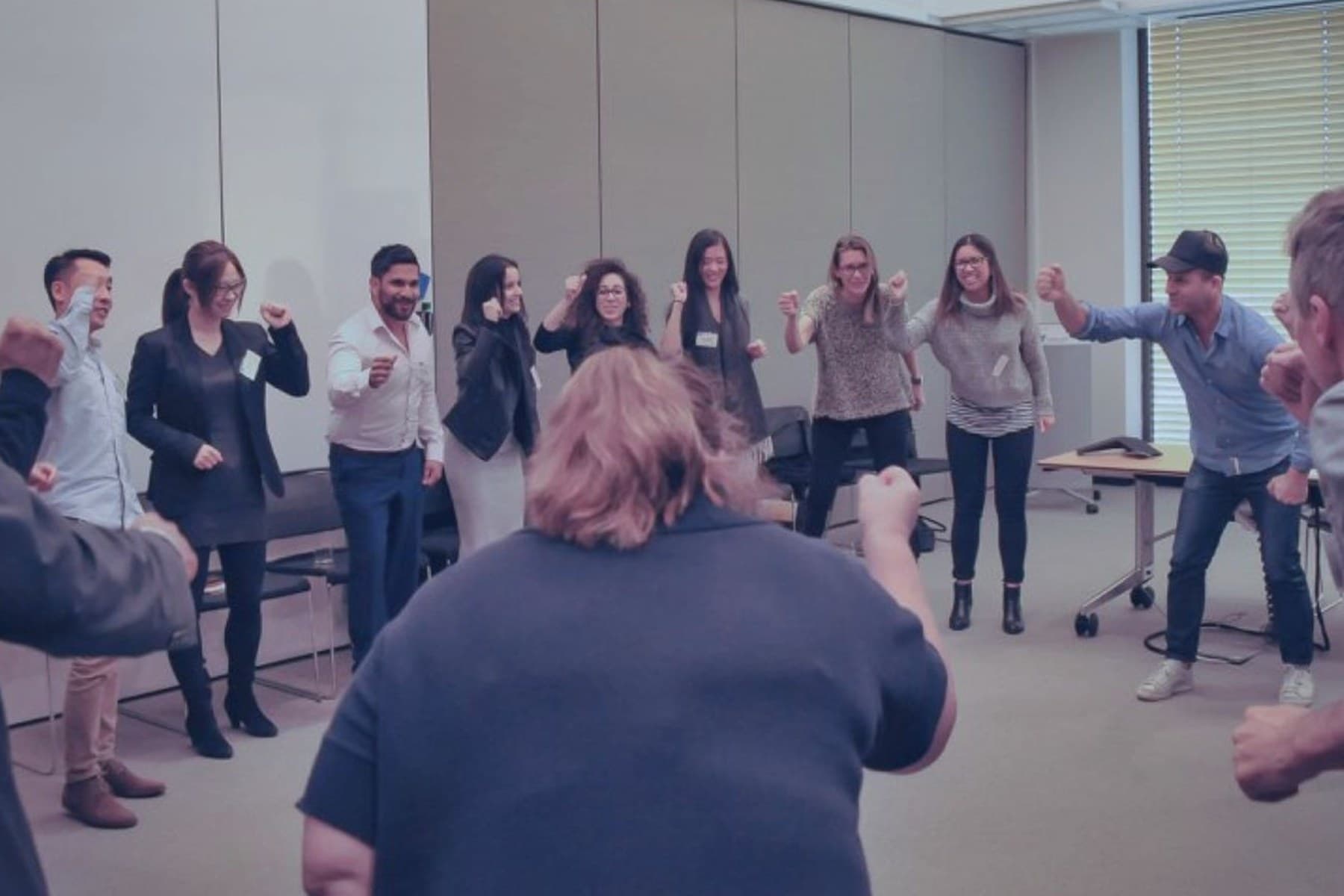 A team standing in a full circle with fists raised at the end of a PowerProv workshop